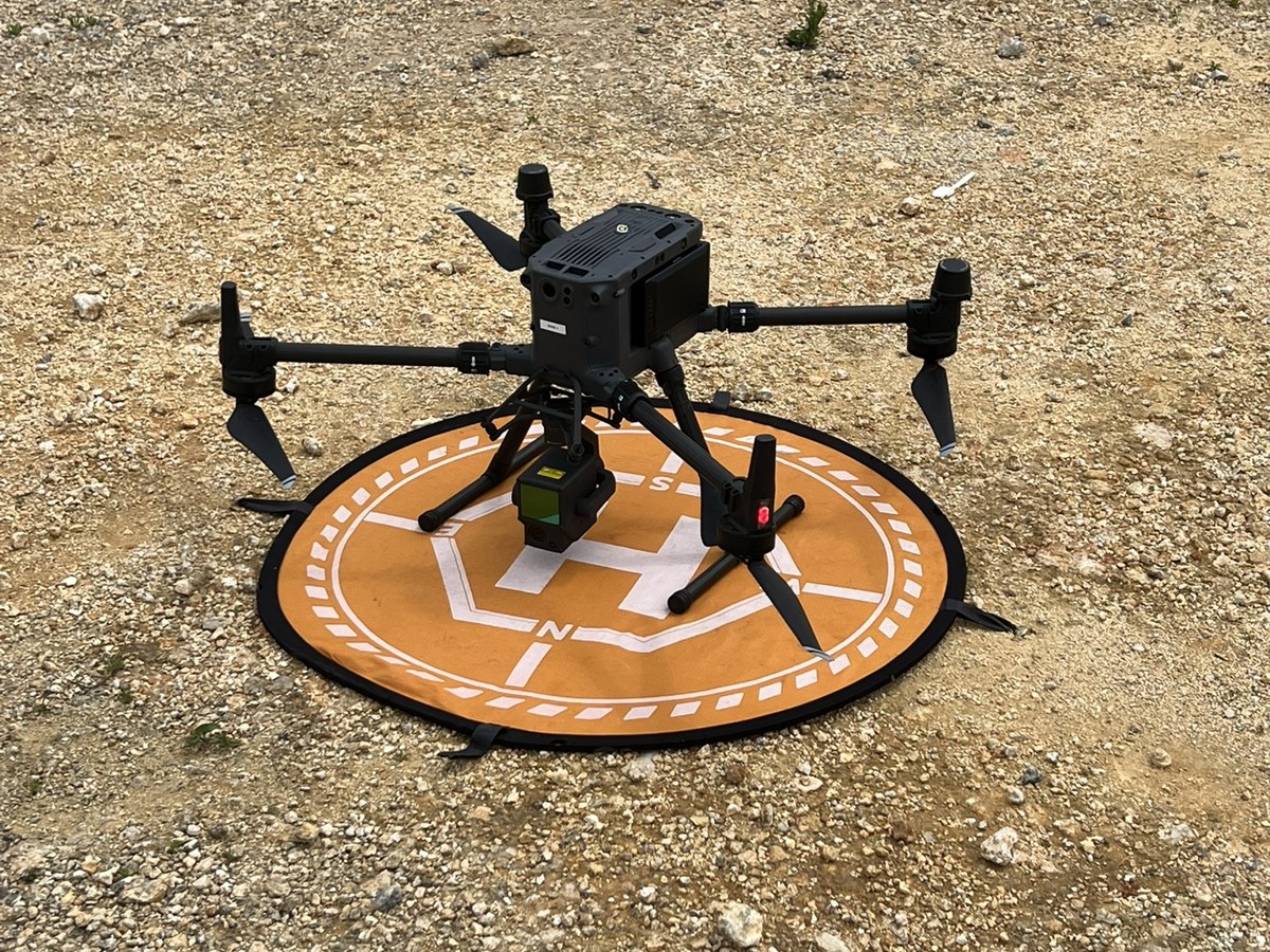 Dron sobre su plataforma de despegue en un terreno de gravilla
