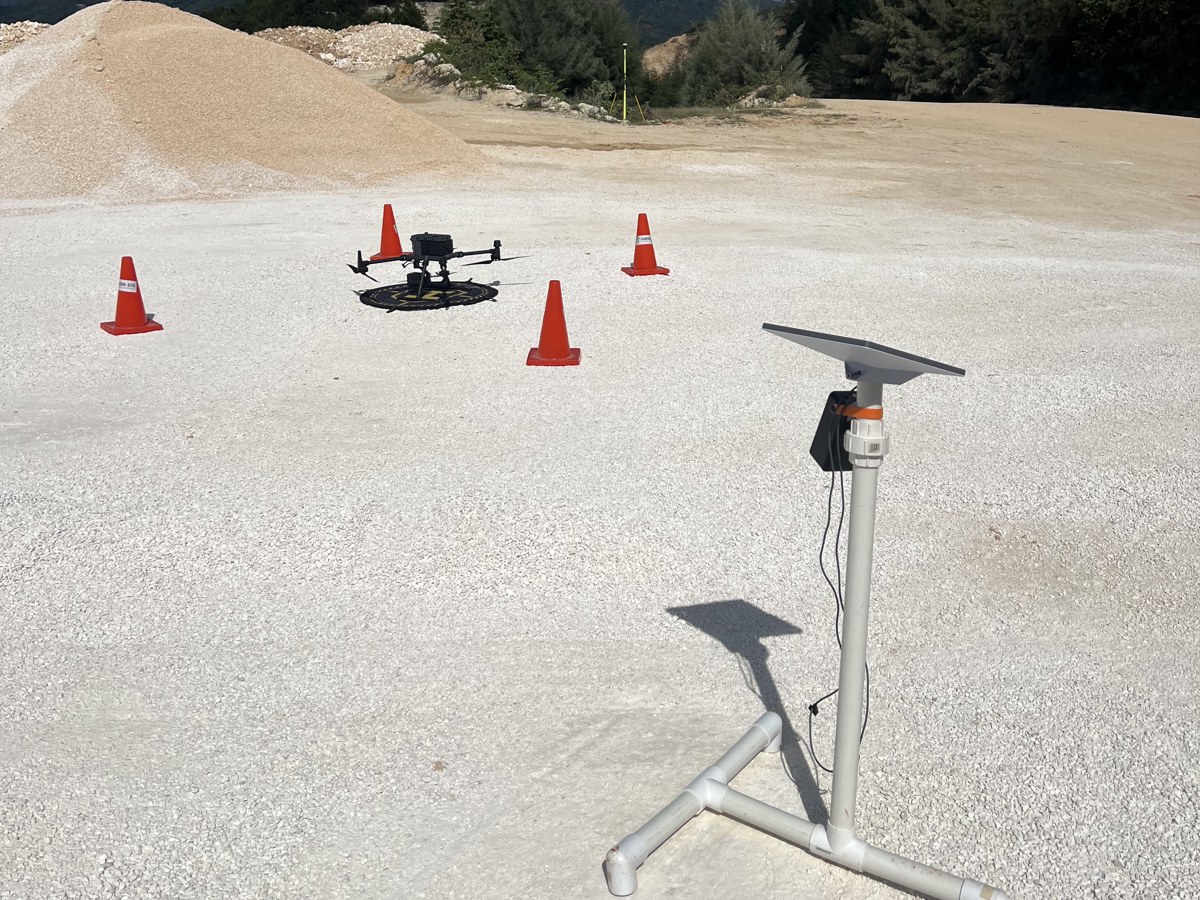 Dron sobre su plataforma de despegue junto a conos y una antena de referencia en una cantera
