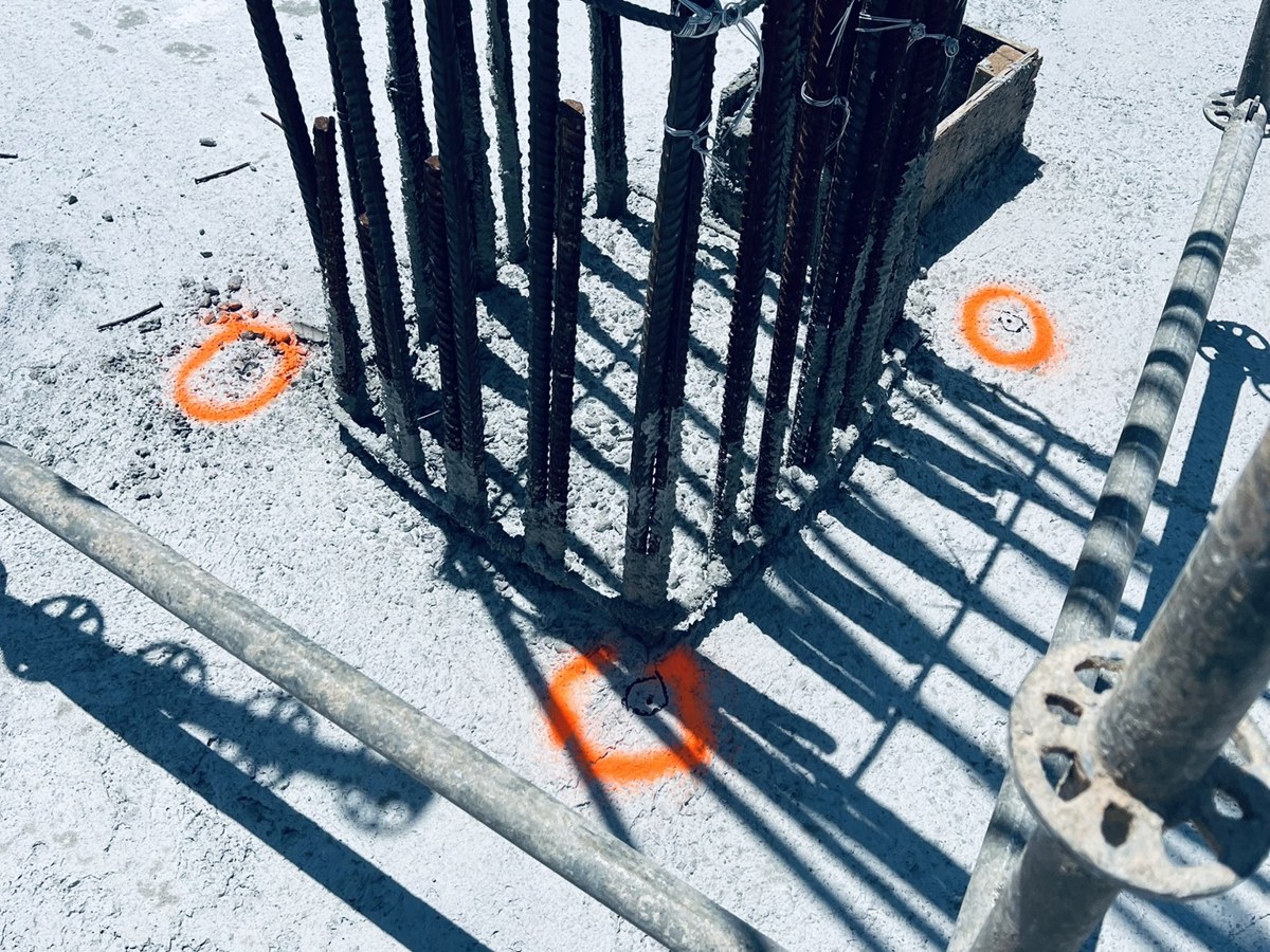 Marcas de replanteo naranjas sobre una losa junto a una columna de varillas y un andamio