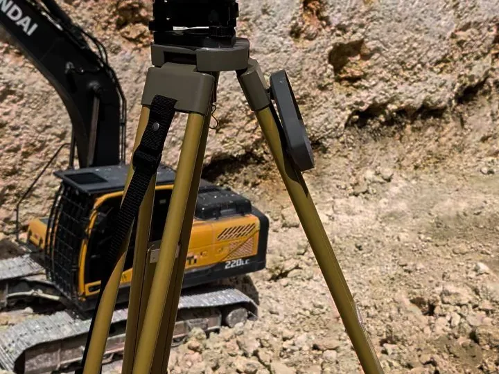 Trípode de la estación total junto a una excavadora durante el movimiento de tierra